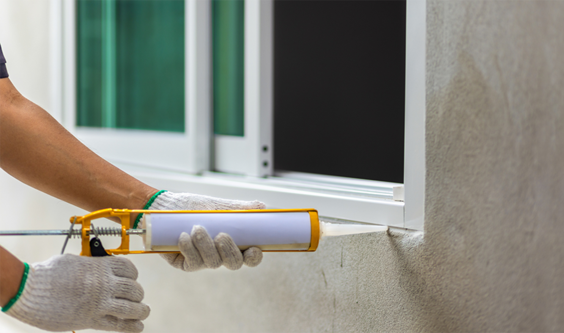 person sealing gap in window